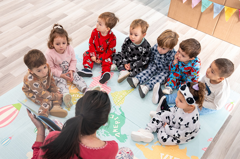 Niños en pijama sentados en círculo sobre una alfombra mirando un libro
